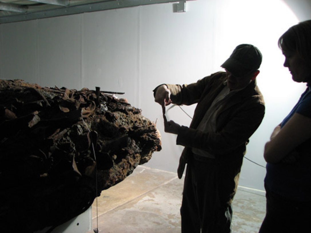 The World Trade Center museum curator shows Col. Dawne Deskins, Eastern Air Defense Sector vice commander, the rock-like mass that was created when four floors of the tower crushed together when it fell. The dim, dramatic lighting casts an eerie glow on the artifact. 