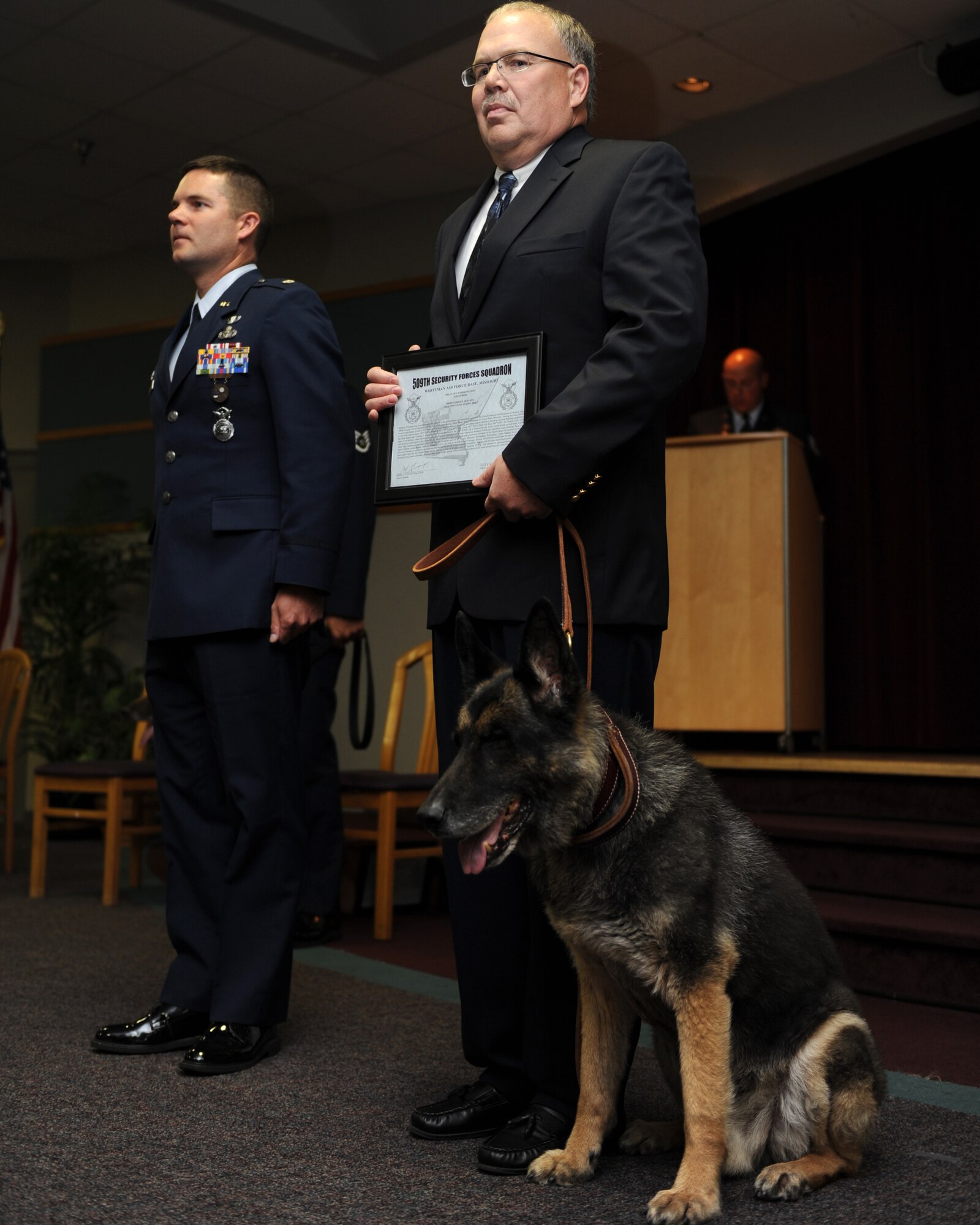 WHITEMAN AIR FORCE BASE, Mo. – Military Working Dog, Joost sits next to his new owner Mark Lenger during his retirement ceremony from active duty, Oct 8. MWDs Charlie, Joost, Rico, and Tina retired from active duty service Oct. 8 after more than 35  combined years of service to their country. (U.S. Air Force Photo/ Senior Airman Cory Todd)