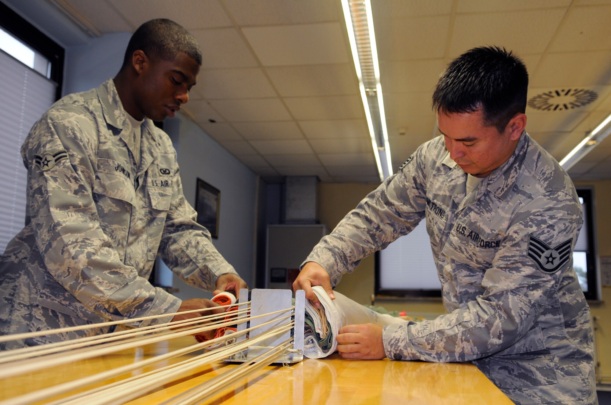 SPANGDAHLEM AIR BASE, Germany – Airman 1st Class Alexander Johnson and Staff Sgt. Ronald Armstrong, both 52nd Operations Support Squadron aircrew flight equipment technicians, fold the canopy of a parachute before packing it Oct. 6. The aircrew flight equipment flight at Spangdahlem is responsible for maintaining about 90 F-16 Fighting Falcon and 27 A-10 Thunderbolt II parachutes. (U.S. Air Force photo/Senior Airman Benjamin Wilson)
