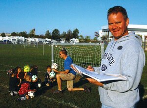 Bob Mowchan, 316th Force Support Squadron Youth Sports and Fitness director, game scheduling paperwork as Bill Lewis, soccer coach, goes over basic soccer fundamentals with a group of Andrews Youth Sports Recreation League soccer team members during a practice at  Field One Monday. (U.S. Air Force photo/ Bobby Jones)