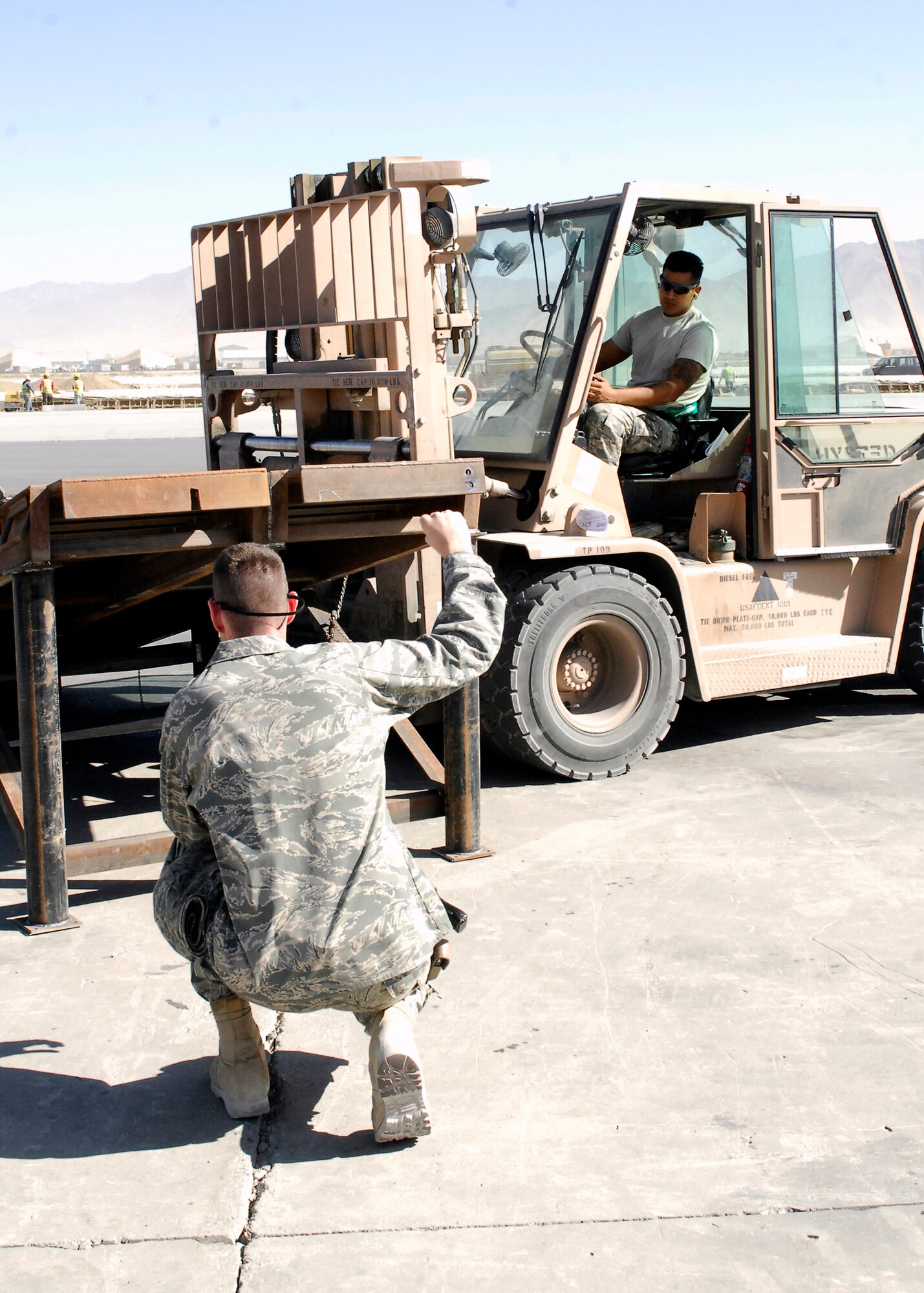 BAGRAM AIRFIELD, Afghanistan -- Captain Bruce Osborn (left), the 455th Expeditionary Aerial Port Squadron Operations Officer, directs Senior Airman Alfred Garcia (driving), a member of the ramp load team from the 455th EAPS, on where he needs to place the ramp here, Oct. 9, 2009.  This mission essential ramp was offloaded and stored on the flightline by the 455th EAPS.  Captain Osborn is deployed from Vance Air Force Base, Okla., and hails from Mangum, Okla.  Airman Garcia, a San Antonio, Texas native, is deployed from Lackland Air Force Base, Texas.  (U.S. Air Force photo/Senior Airman Felicia Juenke)