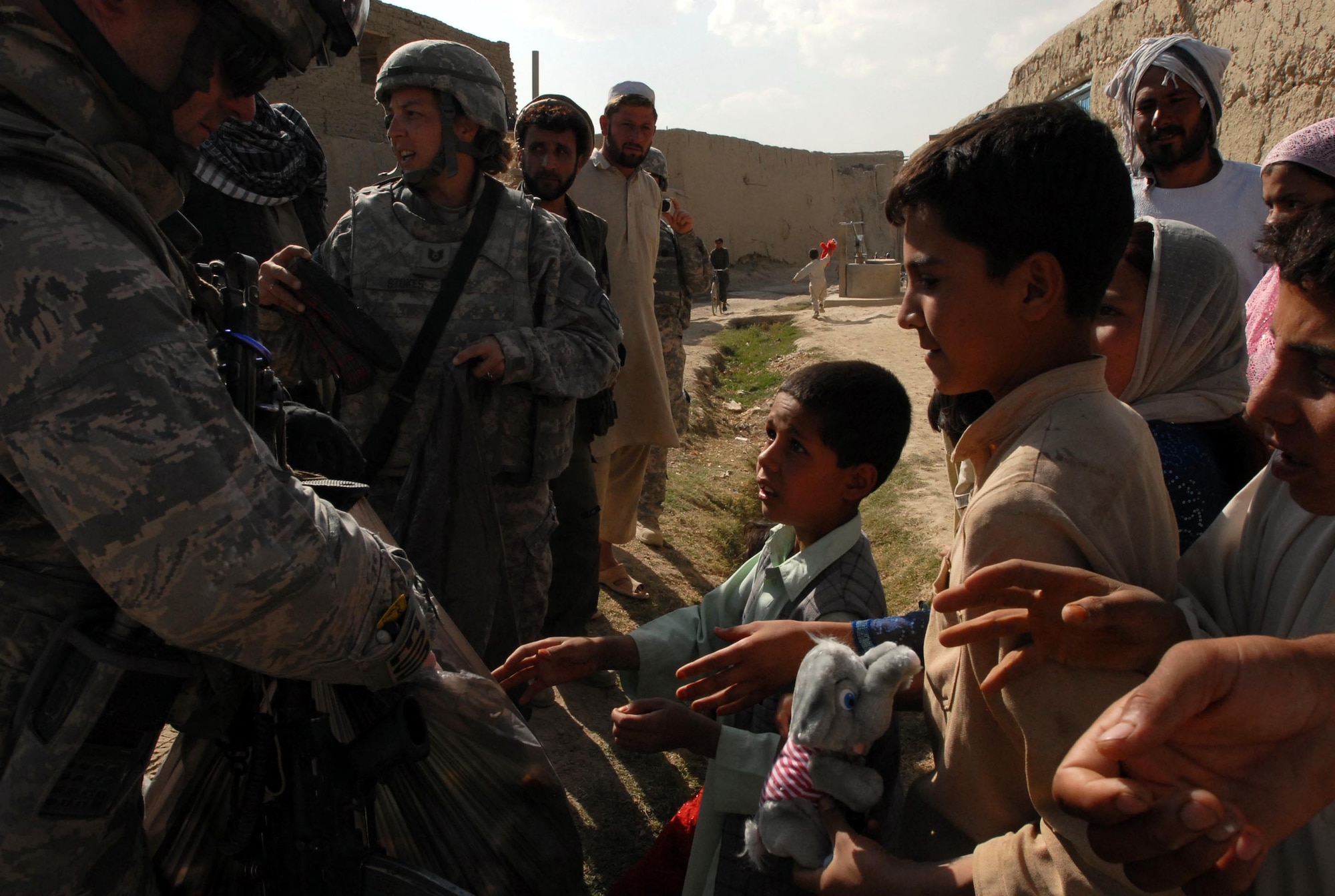 LOGAR PROVINCE, Afghanistan - Tech. Sgts. Michelle Stokes (center) and Brandon Livingstone (left), counter improvised explosive device team, out of Forward Operating Base Shank distribute school supplies, toys and shoes to children in the village of Polerad. (U.S. Army photo/Pfc. Melissa Stewart)