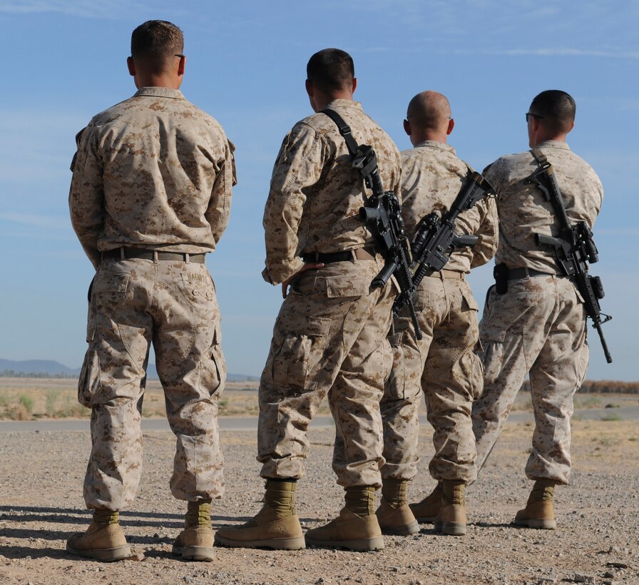 Members of E Company, 2nd Battalion, 7th Marine Regiment, watch aircraft take off in the distance near the flight line at the Marine Corps Air Station in Yuma, Ariz., before a helicopter raid training exercise Oct. 10, 2009. The Marines routinely tuck their blouses into their trousers during helicopter missions to keep the loose material from hanging out. The battalion, based in Twentynine Palms, Calif., is scheduled to deploy with the 31st Marine Expeditionary Unit in early 2010, with E Company assigned to specialize in helicopter insertions and raids.
