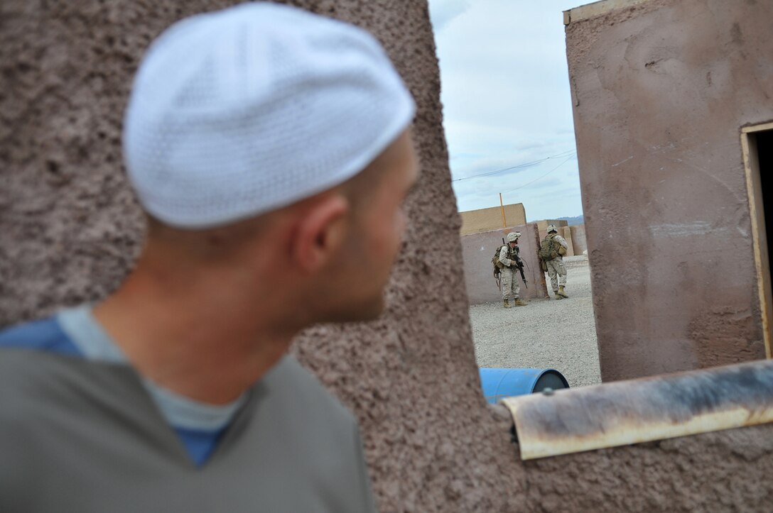 Lance Cpl. Timothy Buckley, an insurgent role player, peeks around the corner of a building as Marines from E Company, 2nd Battalion, 7th Marine Regiment, search for him in the midst of a helicopter-borne raid on a mock Middle Eastern village on U.S. Army Yuma Proving Ground, Oct. 12, 2009. Buckley, along with two other role players, acted as high-value individuals, who were targeted for extraction from the village. The Marines landed in four different locations via UH-1N Huey helicopters around the area and proceeded to clear houses and courtyards in search of their targets.