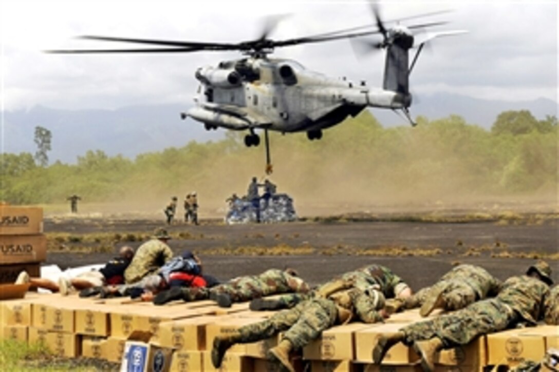 U.S. Marines, airmen and relief agency workers use their body weight to prevent relief supplies from being swept away by the downdraft created by a CH-53E Super Stallion helicopter as crews load it with cargo nets of relief supplies for the regions of Western Sumatra and Padang, Indonesia, Oct. 12, 2009. The helicopter crew is assigned to Marine Medium Helicopter Squadron 265.