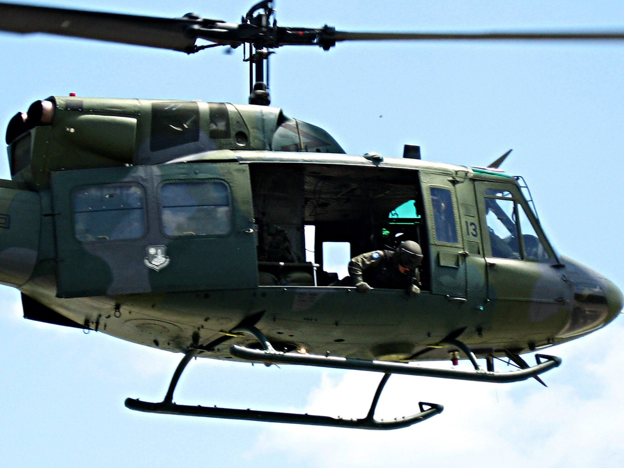A flight engineer with the 36th Rescue Flight here surveys the landscape from a U-H1N Huey helicopter to search for a survivor. (US Air Force photo/ Staff Sgt. Jacob Bragg)
