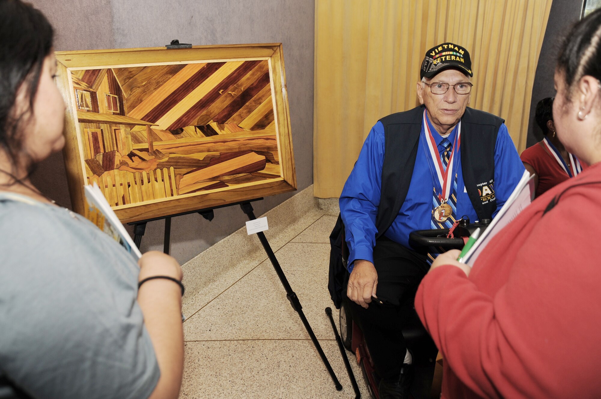 Navy veteran Robert Elling explains his staining techniques to viewers as he sits beside his artwork during the 2009 National Veterans Creative Arts Festival Oct. 11, 2009, at the San Antonio Municipal Auditorium in San Antonio. Mr. Elling uses a staining technique he discovered accidentally when he inadvertently left a piece of steel wool in a jar of vinegar, enabling the vinegar to ?age? the wool.