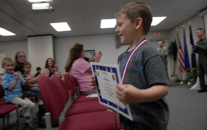 Jordan Thomas smiles as he is applauded during the Little Heros recognition ceremony at the Airman and Family Readiness Center here Oct. 8. The ceremony was held to honor the children of deployed Air Force members and each received a certificate of appreciation and medal. Jordan is the son of Senior Airman Jacob Thomas, vehicle and vehicular maintenance journeyman with the 437th Logistics Readiness Squadron. (U.S. Air Force photo/Staff Sgt. Daniel Bowles)