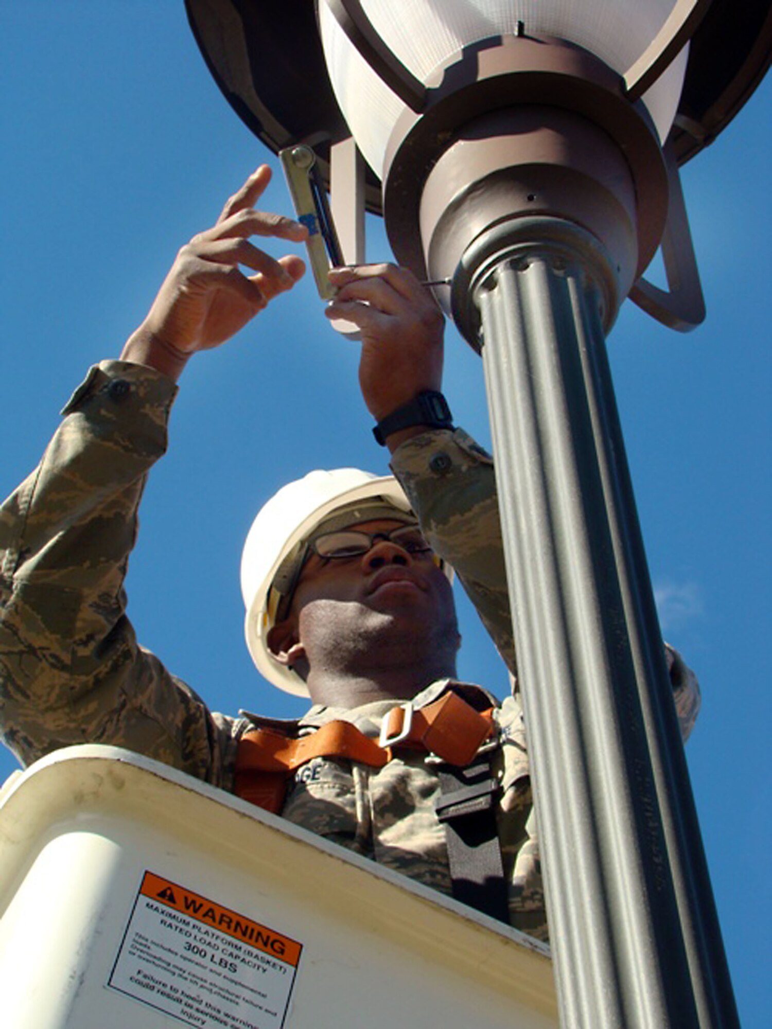 Airman Javier Lodge changes the fastening bolts on a street lamp here at the intersection of West Arnold and Tuskegee Airmen avenues Oct. 8. The current bolts are being replaced with larger bolts, shown by Staff Sgt. Hasheen Maxwell, which are made with a grasping feature. This is the fifteenth lamp out of 400 he and his coworkers will repair and upgrade in light of damage from the recent high winds. The new hardware is intended to prevent further repairs of this kind. Airman Lodge, an electrical systems apprentice with the 87th Civil Engineer Squadron, is from Tampa, Fla. Sergeant Maxwell, an electrical systems journeyman also with the 87th CES, hails from Atlanta. (U.S. Air Force photo by Tech. Sgt. Denise Johnson)