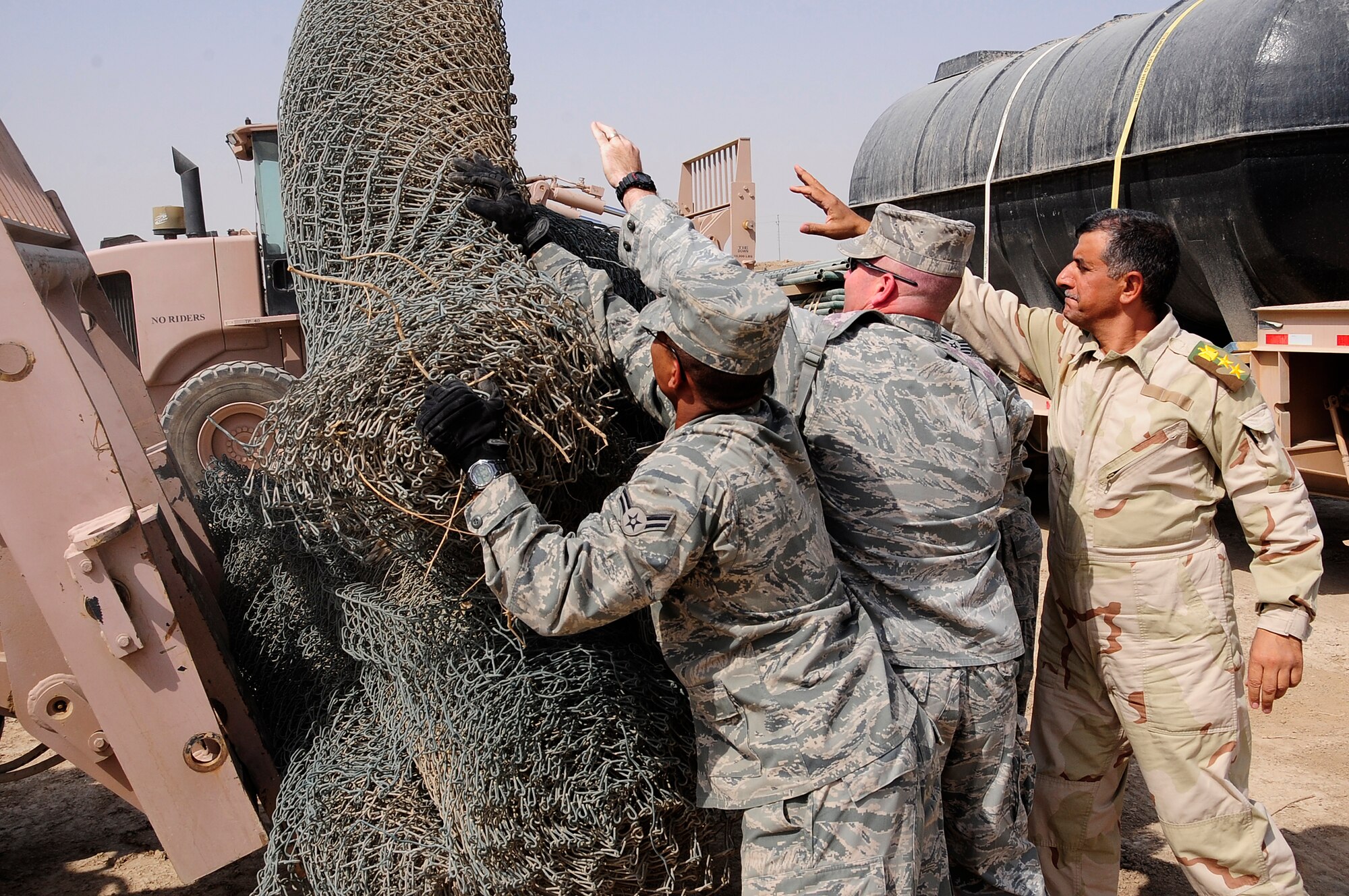 ALI BASE, Iraq - (left to right) U.S. Air Force Airman 1st Class DeMario Greene and  Lt.Col. Derek Scott, Commander, both with 407th Civil Engineer Squadron and Iraqi Army Col. Muhammad Abd Al-Muhssan Khalaf Mahd, Commander, 10th Iraqi Army Division assist in off loading fencing material at Camp Mittica, Iraq, Oct. 14, 2009. The fencing was part of a significant donation of building material made by the squadron to the 10th Iraqi Army Division assigned to Camp Mittica.  (U.S. Air Force photo/Senior Airman Tony R. Ritter)