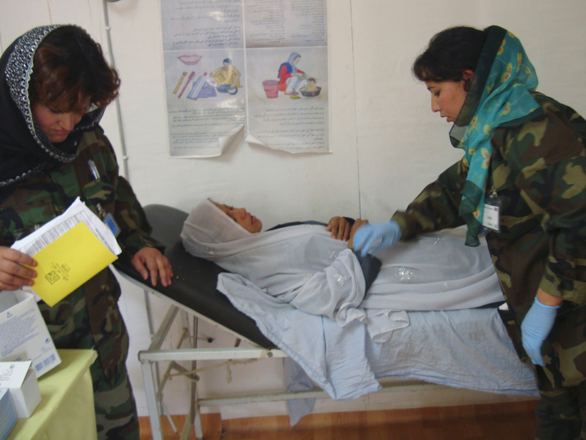 BAGRAM AIRFIELD, Afghanistan -- Malika Faqiri (left) and Laila Farahi (right), two female Afghan National Army soldiers, help with an Afghan woman here. The two nurses attended a special two-week mentorship program here at the Craig Joint Theater Hospital to work alongside U.S. doctors and nurses to hone their medical skills and get first-hand experience with trauma-based care.  The two soldiers were the first women to attend the special program.  (Courtesy photo)