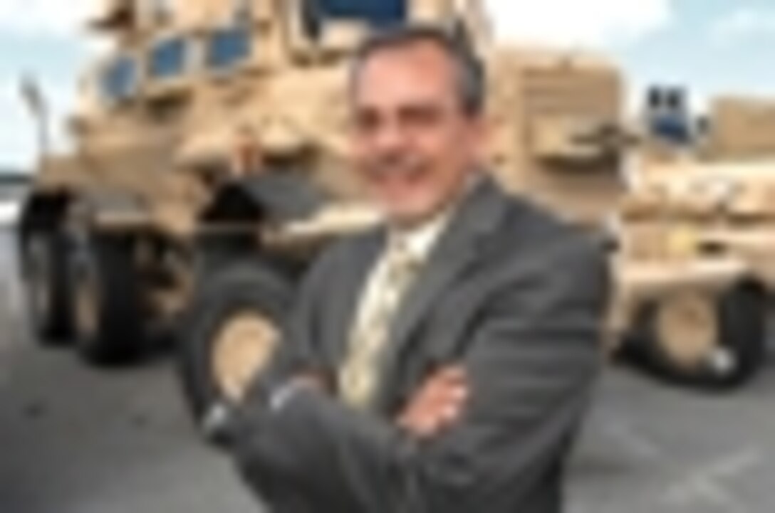 Chris Berry, director, Program Support Division, MRAP Program, Program Support Center, LOGCOM, stands near a Buffalo MRAP vehicle on base.