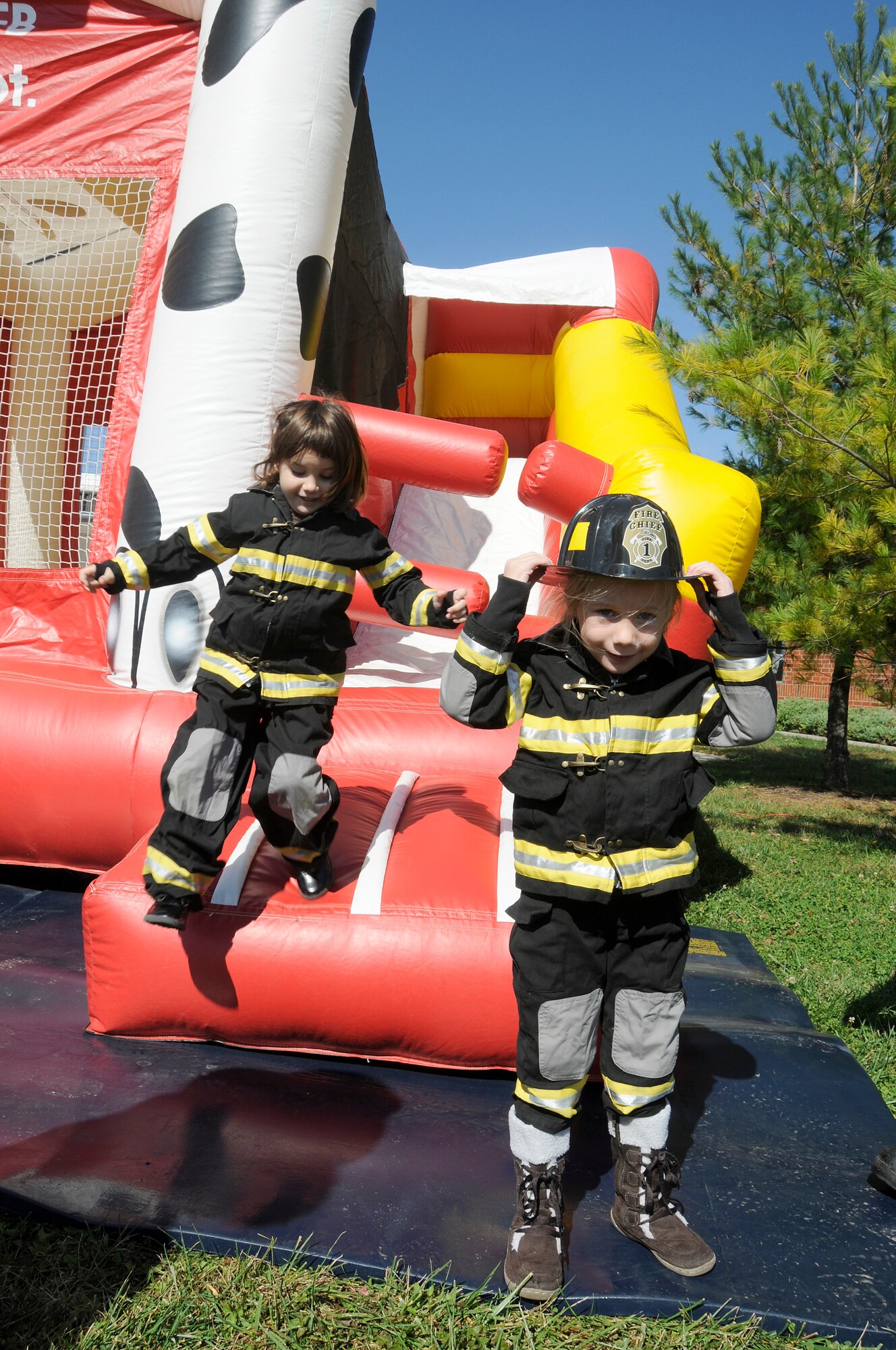 Zoe Leist puts on her "volunteer" firefighter hat as Alexa Leist jumps down from a slide during a children's firefighter challenge at Scott on Saturday. The firefighter challenge was one of many events put on as part of Fire Prevention Week. Zoe and Alexa are the daughters of Petty Officer 2nd Class Andrew Leist, United States Transportation Command.