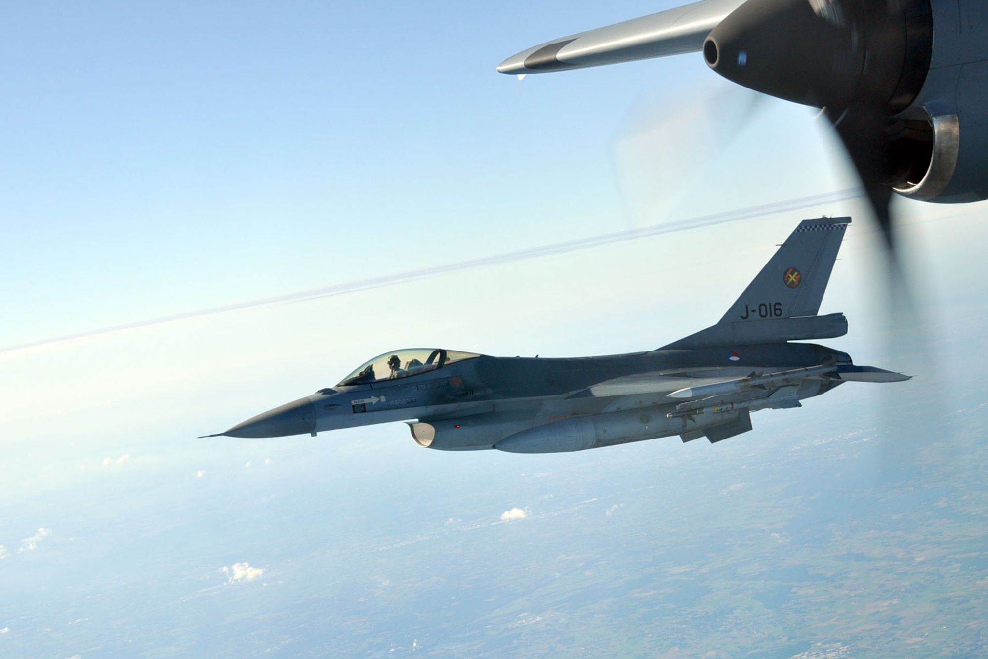 A Royal Netherlands Air Force F-16 ?Fighting Falcon? jet fighter interceptor flies just off the wing of a C-130H ?Hercules? tactical cargo transport aircraft from the Air Force Reserve?s 910th Airlift Wing during a flight from Prestwick, Scotland to Ramstein Air Base, German, October 14. The fighter was scheduled to meet the C-130 as it flew from over the North Sea into Ducth air space. The C-130, based at Youngstown Air Reserve Station, Ohio, was carrying a group of Citizen Airmen bound for Ramstein in support of Operation Joint Enterprise. The C-130 crews and maintainers participating in Joint Enterprise will work together to airlift cargo to locations in the U.S. Europe Command (EUROCOM) and the U.S. Africa Command (AFRICOM) Theaters of Operation. U.S. Air Force photo by Master Sgt. Bob Barko Jr.
