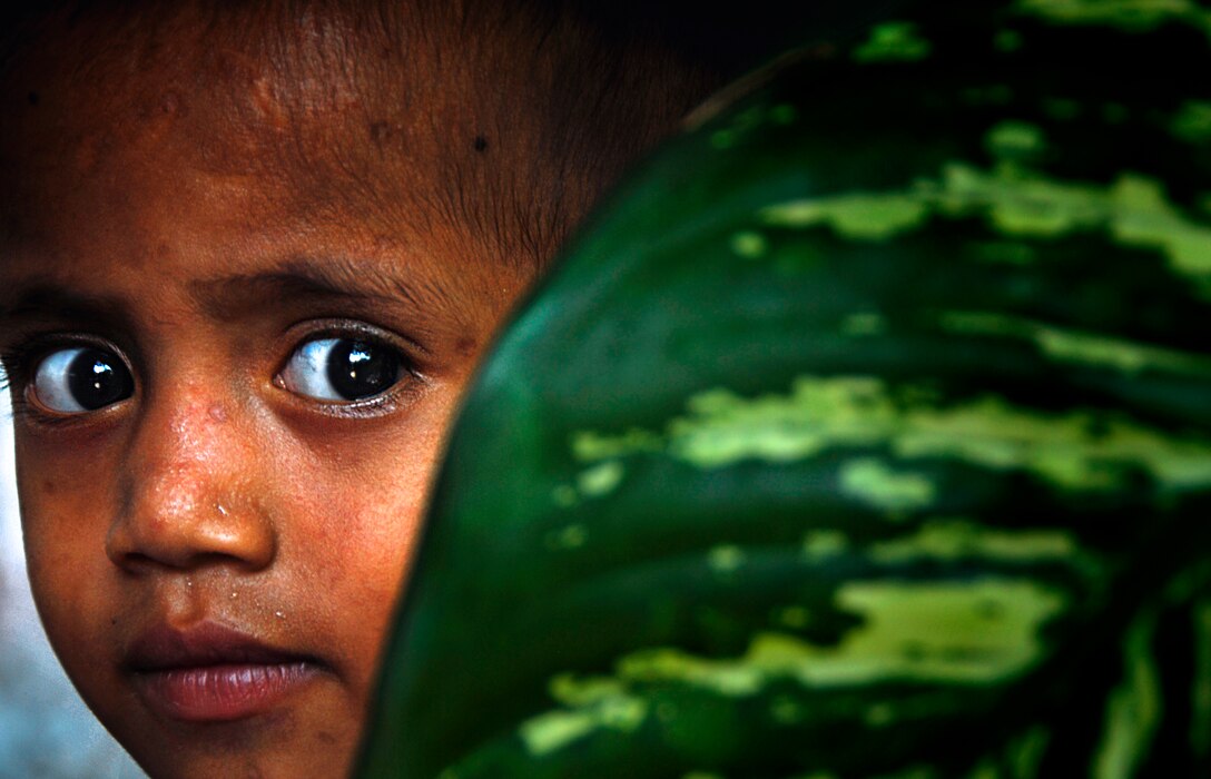 An orphan peers from behind a plant at the Santa Clara Orphanage here Oct. 17 where Marines with the 11th Marine Expeditionary Unit were delivering bottled water.