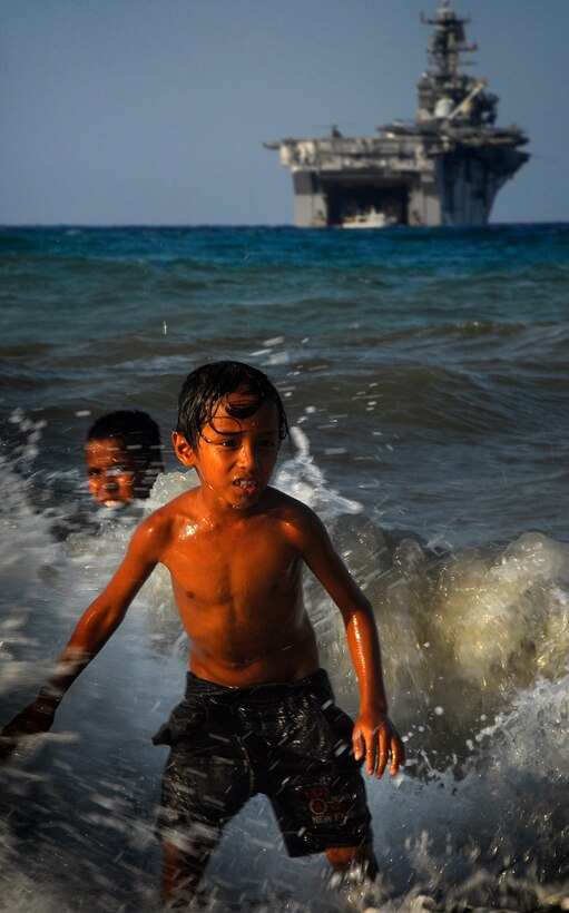 Local boys swim at the beach here Oct. 17 as the amphibious assault ship Bonhomme Richard sits anchored in the background. Aboard the ship are members of the 11th Marine Expeditionary Unit, in the country conducting jungle and urban training with other militaries and performing medical, dental, engineering, and community projects.