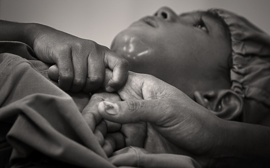 A 4-year-old boy grips his mother's hand before undergoing surgery to remove decayed teeth and drain an infection in his neck at Santa Rosa Hospital in Oecussi, Timor Leste, Oct. 17. Navy Lt. Billy Turley, a general dentist with the 11th Marine Expeditionary Unit and Auburn, Ky., native, performed the surgery.