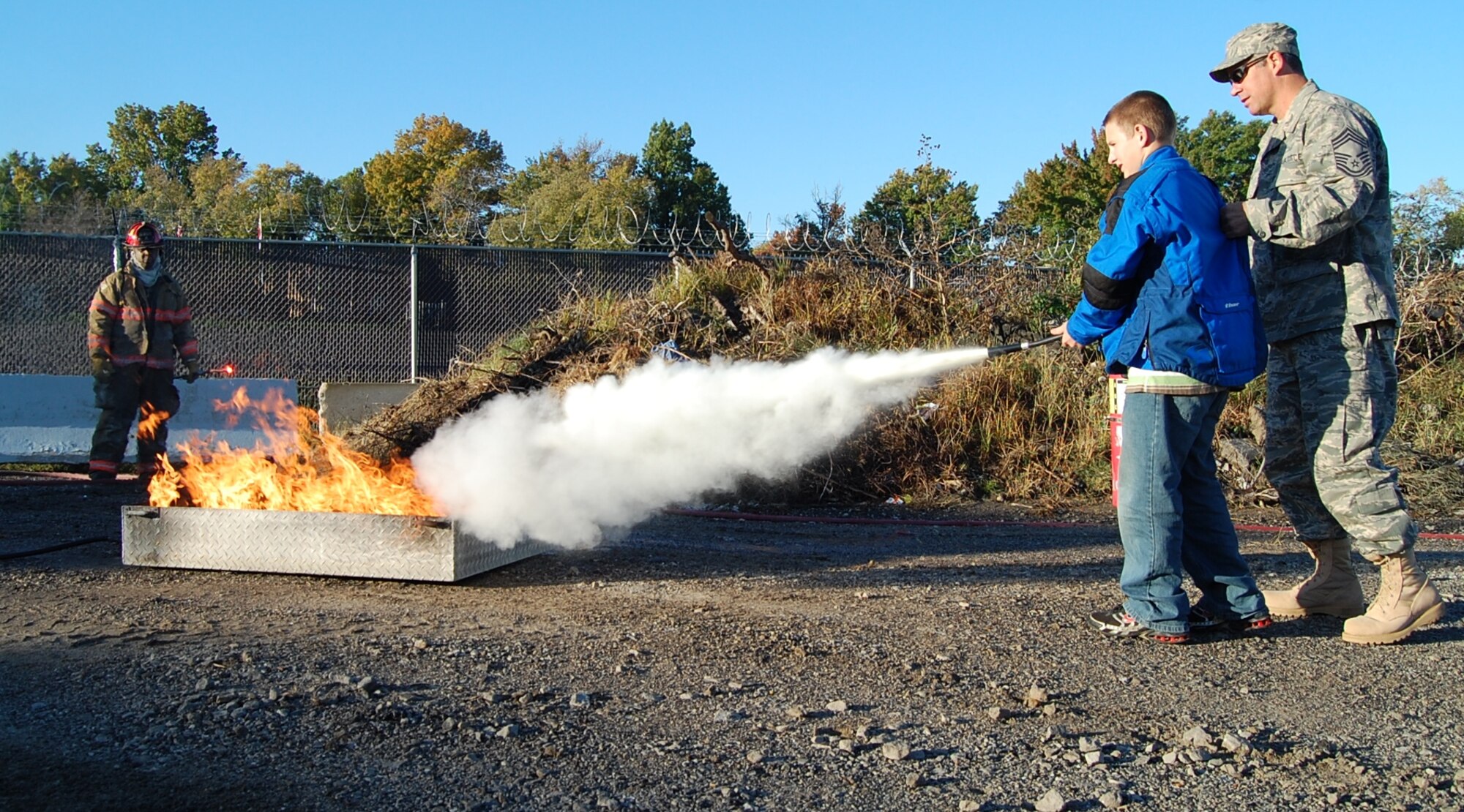 Chief Master Sgt. Tim Hill, 231st Civil Engineer Flight fire chief, teaches his son, Zach Hill, how to properly use a fire extinguisher to put out a fire Oct. 18. The 231st teamed up with a local fire department to help teach servicemembers fire safety in honor of Fire Safety Month. (Photo by Senior Airman Jessica Donnelly)