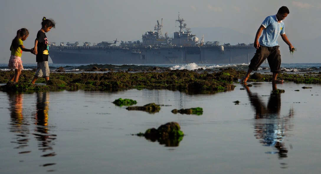 With the amphibious assault ship Bonhomme Richard anchored in the background, a Timor Leste man gathers fishing bait at a tide pool here with his family Oct. 18. Aboard the ship are members of the 11th Marine Expeditionary Unit, in the country conducting jungle and urban training with other militaries and performing medical, dental, engineering, and community projects.