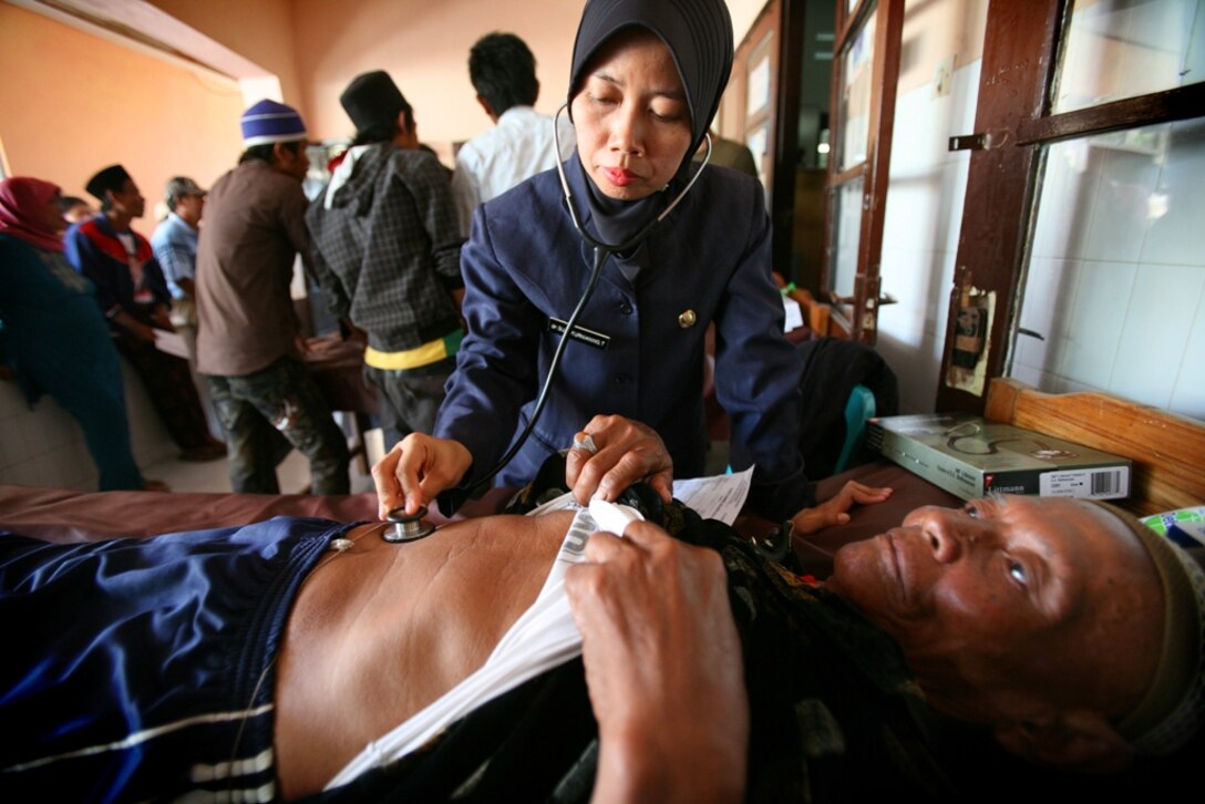 An Indonesian nurse examines an elderly patient alongside Navy medical personnel with the 11th Marine Expeditionary Unit here Oct. 19. Medical personnel treated over 1000 people Oct. 19-21 as part of a medical assistance program. Members of the 11th MEU are in Indonesia for an exercise focused on medical and dental assistance, engineering projects and military interaction.