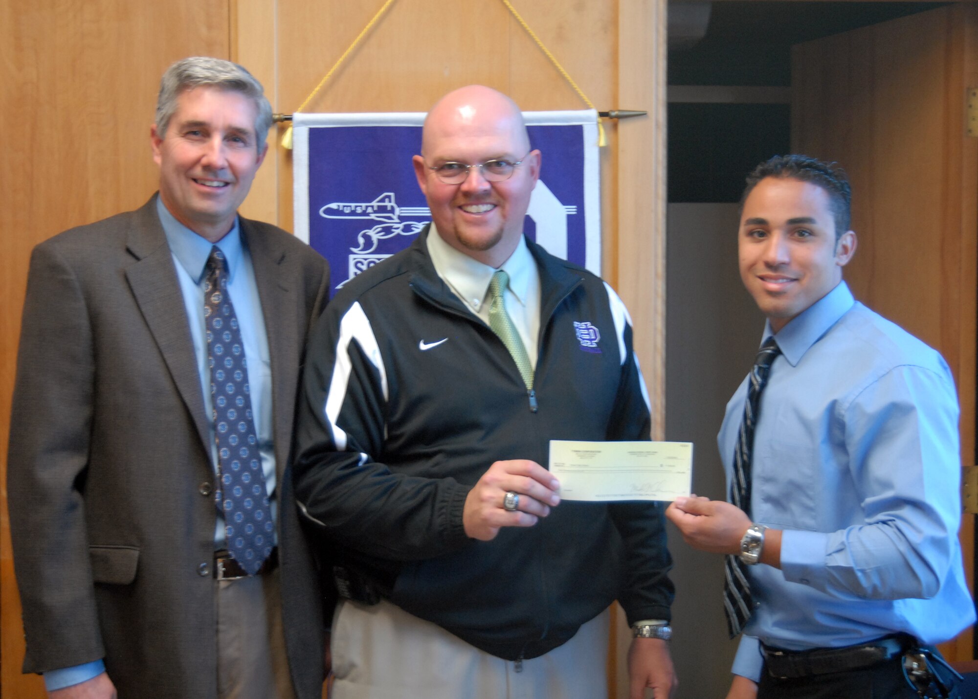Michael Chesebrough (left), TYBRIN Systems Engineering Group director and Troye Fontenette (right), TYBRIN acquisition manager donate $1,000 to Nat Adams (center), Desert High School principal. The donation will be used to fund sports programs which were not funded by Muroc Joint Unified School District (Air Force photo/Airman 1st Class William O'Brien)