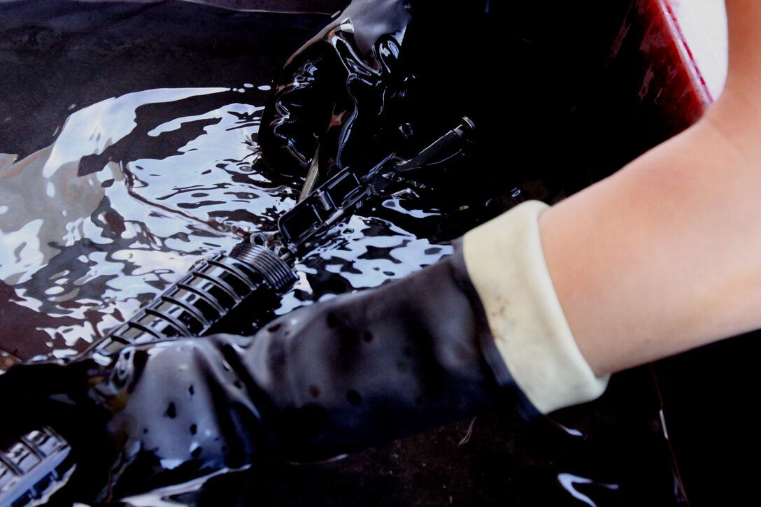 Lance Cpl. Jared N. McDonald, safety noncommissioned officer for hazardous materials, Headquarters and Support Battalion, Marine Corps Base Camp Pendleton, submerges his weapon in a new weapon cleaning solvent named QSOL 300. The solvent is cleaner for the environment and breaks down carbon and other contaminants faster than previously used products.