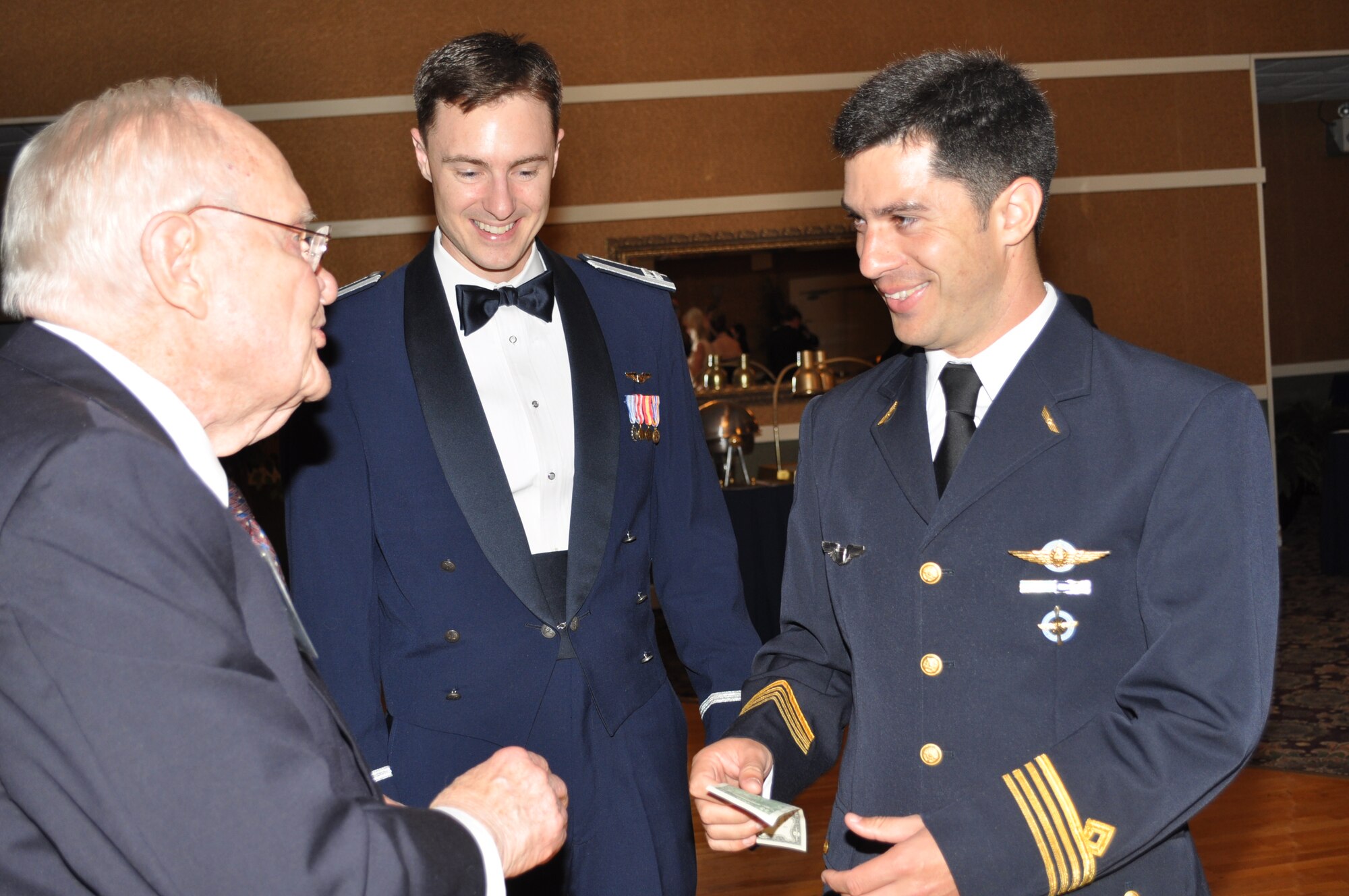 Capt. Mariano Triulzi  and Capt. Christopher Clark of the 49th Fighter Training Squadron talk with Mr. Frank Mullinax, 49th WWII P-38 pilot and former POW, at the 49th Fighter Squadron Association banquet.  Mr. Mullinax traditionally presents members of the 49th a two dollar bill. (U.S. Air Force photo/Sonic Johnson).