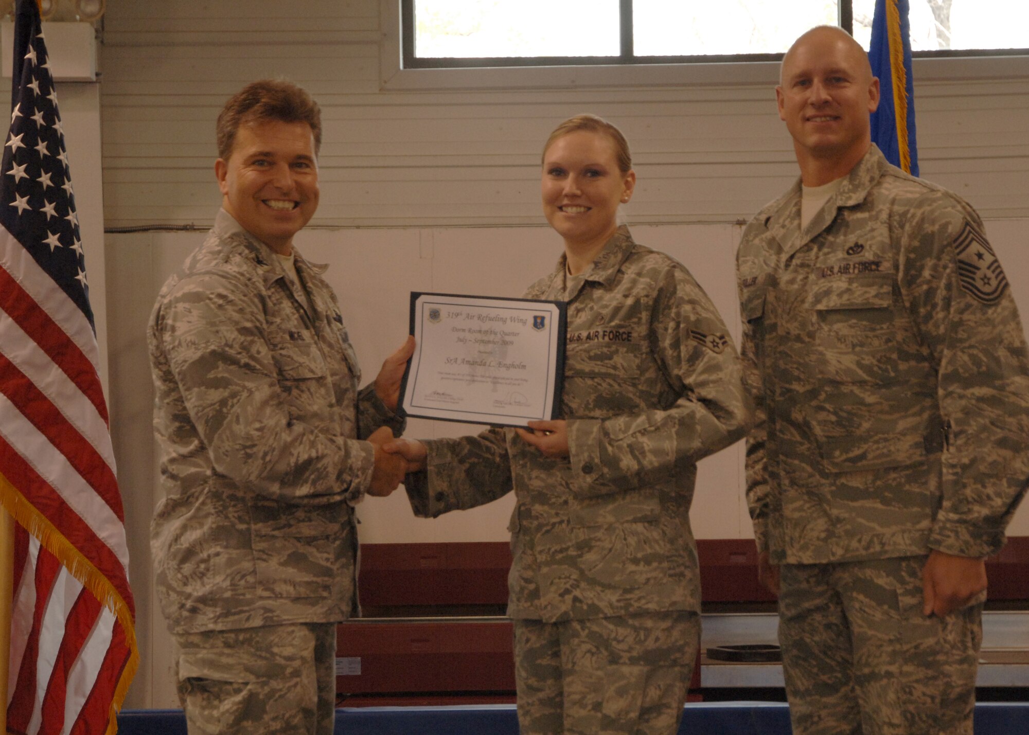Col. John E. Michel, 319th Air Refueling Wing commander, hands the Dorm of the Quarter award to Airman 1st Class Amanda L. Engholm, 319th Medical Operations Squadron, while Chief Master Sgt. Scott A. Fuller, 319th ARW command chief, looks on, Oct. 19 at the wing’s quarterly award ceremony. (U.S. Air Force photo by Senior Airman R. Michael Longoria)