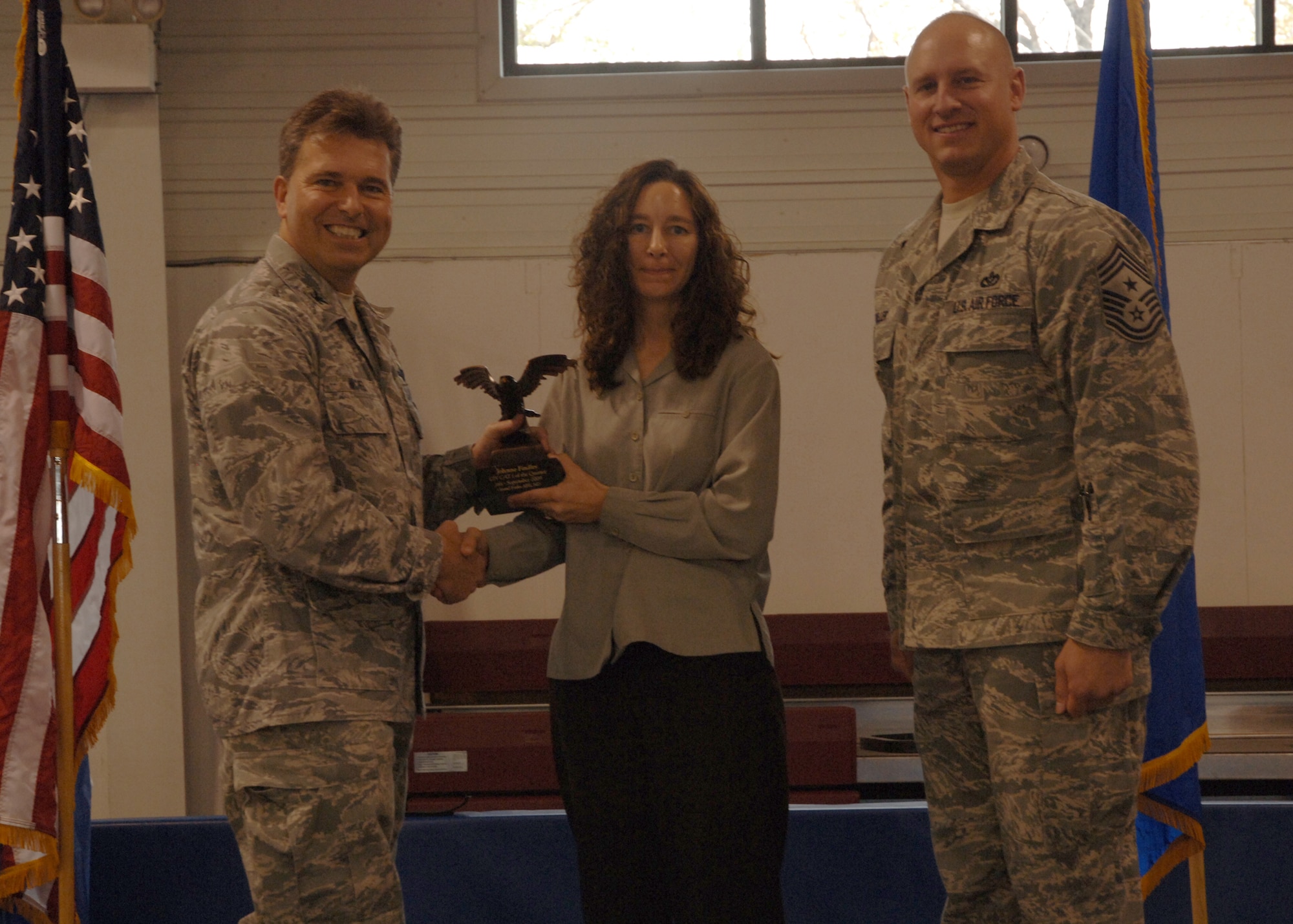 Col. John E. Michel, 319th Air Refueling Wing commander, hands the Category I Civilian of the Quarter award to Jolynne M. Findley, 319th Operations Support Squadron, while Chief Master Sgt. Scott A. Fuller, 319th ARW command chief, looks on, Oct. 19 at the wing’s quarterly award ceremony. (U.S. Air Force photo by Senior Airman R. Michael Longoria))