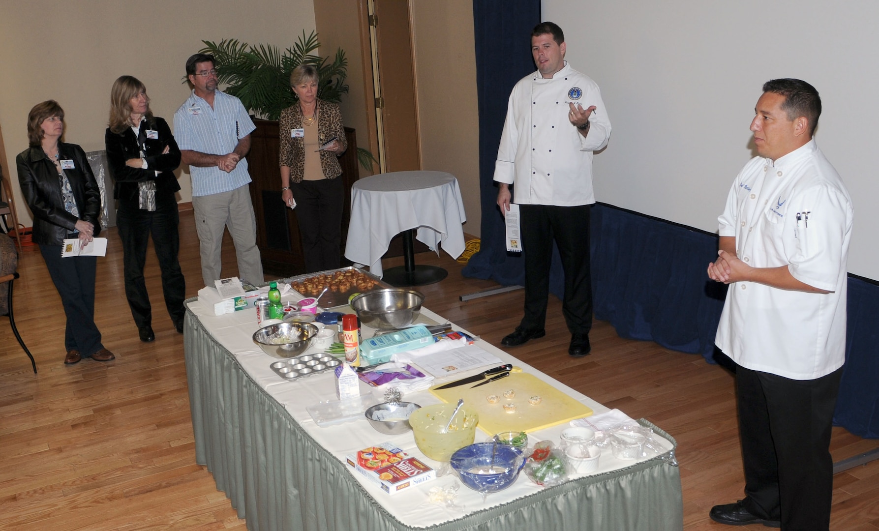 Master Sgt. Greg Krems, center, enlisted aide to the Air Education and Training Command commander, and Tech. Sgt. Raul Martinez, enlisted aid to the Air Armamant commander, explain to spouses attending the AETC Commanders, Command Chiefs and Spouses conference at Randolph Air Force Base how they are going to make an appetizer during the Appetizer Demonstration at Randolph's Parr O' Club. (U.S. Air Force Photo By Don Lindsey)