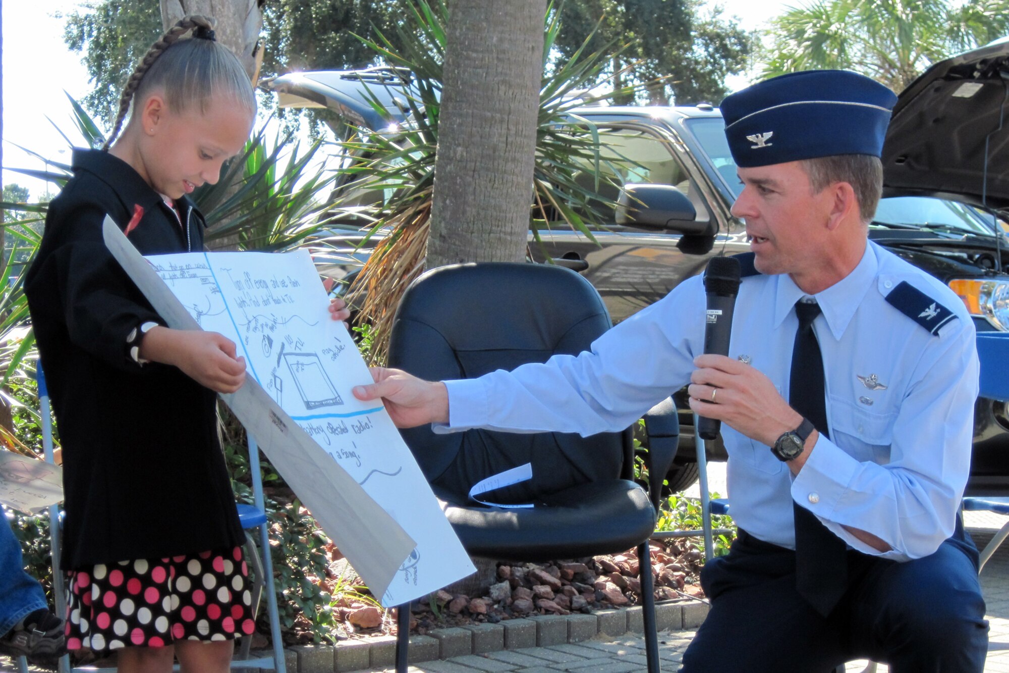 Jasmine Rodden, Eglin Elementary fourth grade poster contest winner, holds her poster while Col. Bruce McClintock, 96th Air Base Wing commander, reads it for the crowd attending Eglin’s Energy Expo, Oct. 21. (U.S. Air Force photo/Mike Spaits)