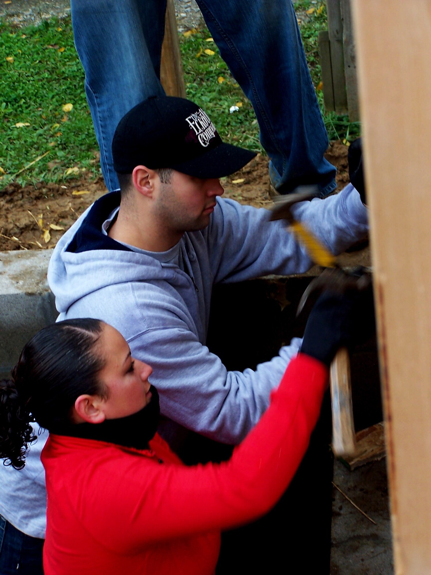 Senior Airman Jamie Rivera (rear) and Airman First Class Kira Namauu (front) hammer nails to secure the outside walls to the front of the Habitat for Humanity house.