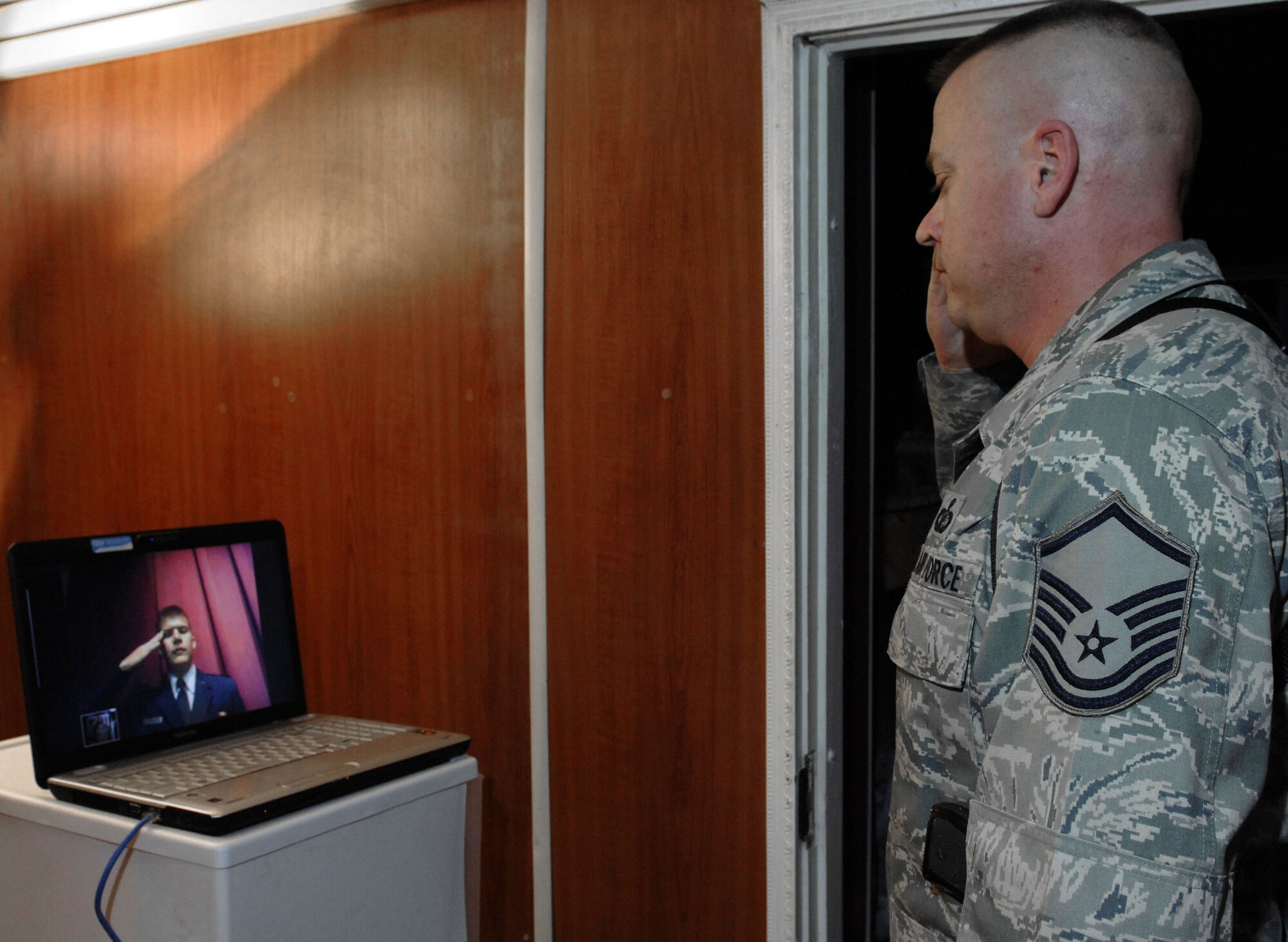 Using a satellite hookup, Master Sgt. Roger Nelson renders the first salute to his brother, 2nd Lt. Bryon Kroger, Oct. 27, 2009, from Camp Eggers, Afghanistan, following Lieutenant Kroger's commissioning during the Officer Training School graduation at Maxwell Air Force Base, Ala.  Sergeant Nelson is a budget analyst deployed from Shaw AFB, S.C. and calls Granite Falls, Minn., home.  Lieutenant Kroger goes on to Goodfellow AFB, Texas, for intelligence school training and hails from Cherokee, Iowa.  (U.S. Air Force photo/Staff Sgt. Larry E. Reid Jr.)