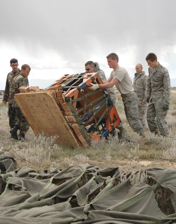Cadets Second Class Benjamin Tyler and Evan Lomeli (left) look on as members of the 39th Aerial Port Squadron turn over a recently-air dropped cargo pallet after a simulated container delivery system drop Sept. 24 at Fort Carson, Colo. The drop, conducted by a C-130 Hercules crew assigned to the Air Force Reserve's 302nd Airlift Wing, supported the U.S. Air Force Academy's Airdrop Enhanced Logistics Visibility System prototype system that demonstrated the ability of commanders in the field and at the headquarters level to simultaneously identify the location and contents of a CDS within minutes of the cargo leaving the aircraft. The AELVIS program aims to provide war fighters in locations like Iraq and Afghanistan with exact details on crucial cargo drops for resupply. (U.S. Air Force photo/Capt. Jody L. Ritchie)