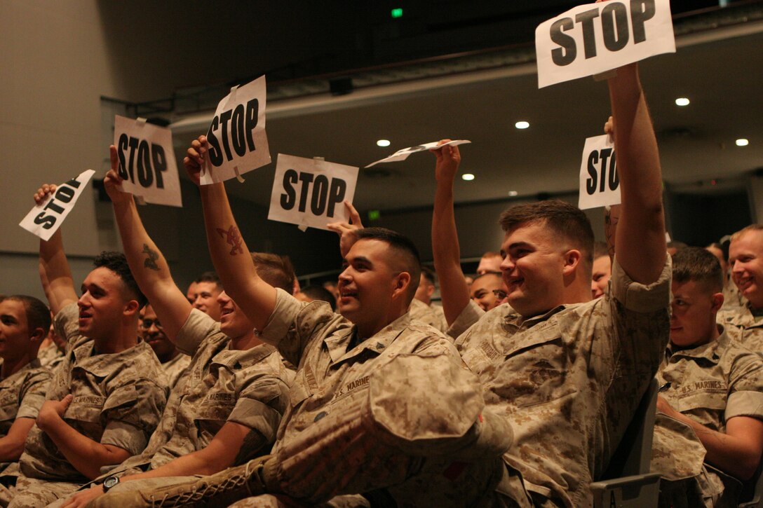 Marines hold up 'Stop' signs during the comedic play 'Sex Signals' at the Base Theater, Oct. 27. Actors in the play acted out various scenarios in which the male actor makes unwanted physical contact with the female character. The Marines held up signs to signal when the aggressor had bordered on sexual assault. The goal of the play was to help service members understand what consent is and that 'no means no.'
