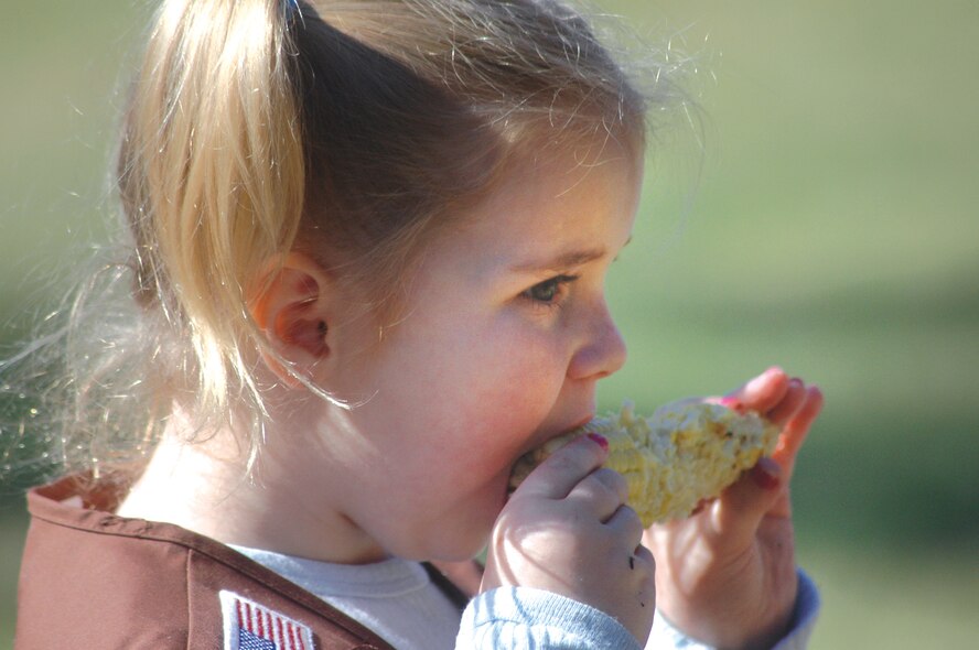 Ashlyn Cox, 6, enjoys some roasted corn on the cob at the primitive skills demonstration.U. S. Air Force photo by Sue Sapp  
