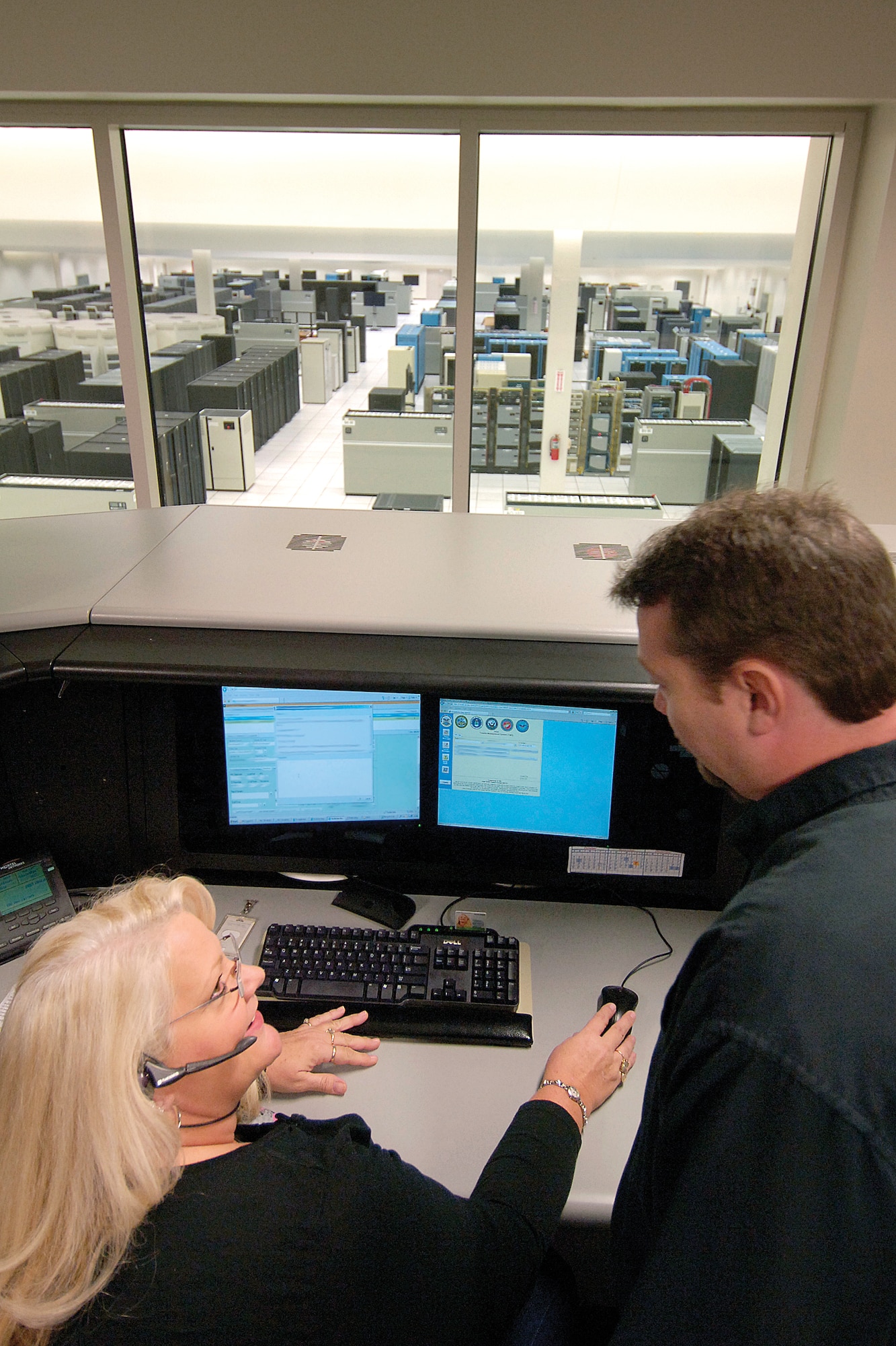 From their work stations overlooking DISA’s main computer room, customer support professionals Sandy Hening and Mikell Spencer help clients worldwide. (Air Force photo by Margo Wright)