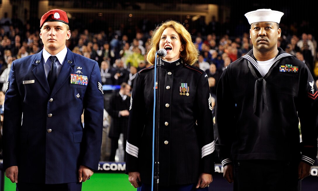 U.S. Army Sgt. Mary Kay Messenger sings "God Bless America" while veterans U.S. Air Force Staff Sgt. Jesse Schrader and U.S. Navy Petty Officer 2nd Class Damion Salabie stand at attention during the first game of the World Series between the Philadelphia Phillies and the New York Yankees at Yankee Stadium in New York, Oct. 28, 2009.