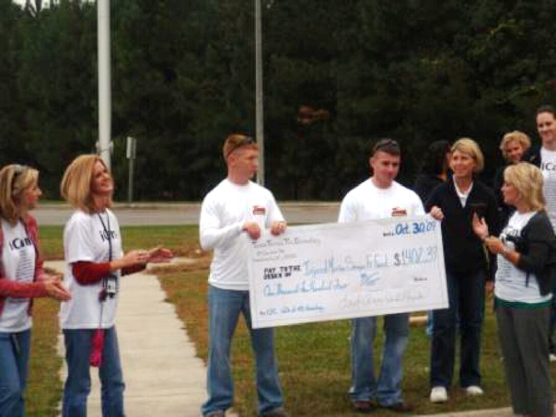 Ms Leigh Anne Kapiko, Principal at TT II Elementary School presents a check for $1,402.39 to Injured Marines Semper Fi program representatives during an assembly at TT2 of Marine Corps Base Camp Lejeune, Oct. 30.