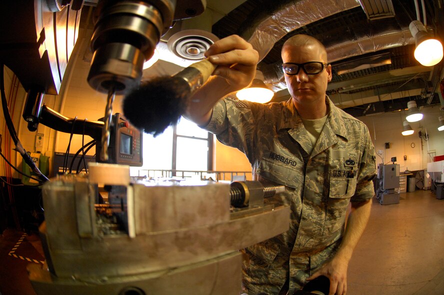 MINOT AIR FORCE BASE, N.D. -- Staff Sgt. Sgt Daniel Hubbard, 5th Maintenance Squadron aircraft metals technology craftsman, brushes excess shards away after drilling holes into stainless steel for a bomb bay door pin puller here Aug. 31. Aircraft metal technicians design, weld, fabricate, and locally manufacture tools, for components and assemblies essential to aerospace weapon systems and related support equipment. (U.S. Air Force photo by Airman 1st Class Jesse Lopez)