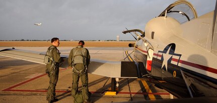 Maj. David Reynolds, T-6 Texan II Instructor Pilot with the 559th Flying Training Squadron, Randolph Air Force Base Texas, looks on as Capt. Andrew Walker, Pilot Instructor Training student with the 84 FTS Laughlin Air Force Base, Texas, prepares for preflight prior to a T-6 training flight involving formation flying, instrument flying, and acrobatics. (U.S. Air Force photo/Steve Thurow).
