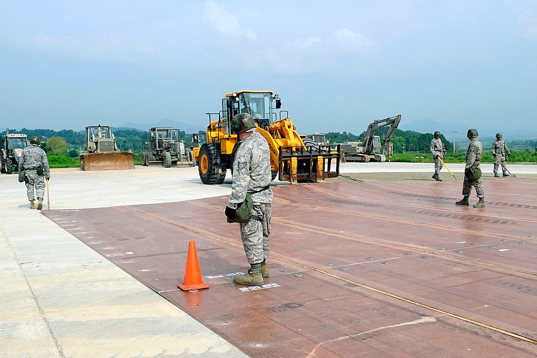 U.S. Air Force airmen stand on a folded fiberglass mat as it is moved into place by a 10,000-pound forklift on a simulated runway on Jungwon Air Base, South Korea, Aug. 19, 2009. The airmen are assigned to the 51st Civil Engineer Squadron on Osan Air Base, South Korea. The 30-foot long, 54-foot wide mats, used to quickly repair runway damage, are being moved during an exercise with airmen from the South Korean air force.