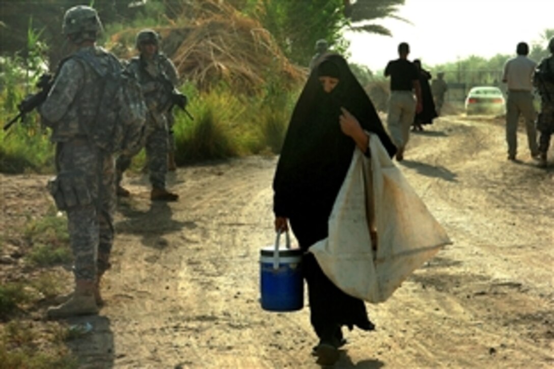 An Iraqi woman walks between soldiers as they pull security for a mission outside Scania Base, Iraq, Aug, 19, 2009. The mission was to check on the condition of a water treatment facility, which filters water for six nearby villages. The soldiers are assigned to Company A, 2nd Battaltion, 162the Infantry Regiment, 41st Infantry Bridage Combat Team, Oregon Army National Guard.