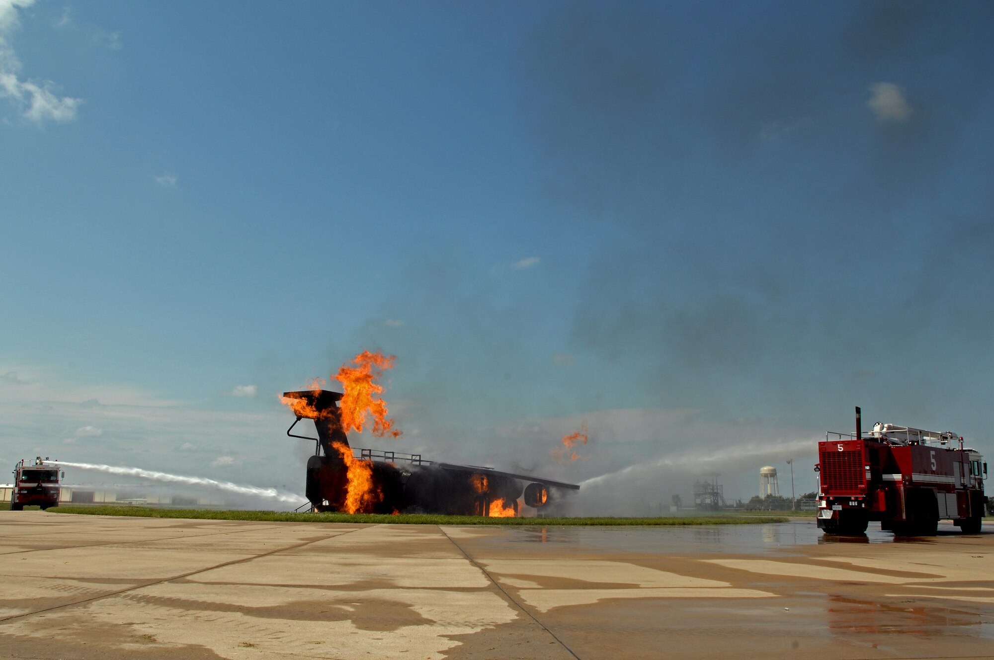 WHITEMAN AIR FORCE BASE, Mo. - Two 509th Civil Engineer Squadron fire trucks circle a flaming aircraft trainer while deploying several gallons of water in an attempt to exstinguish the burning aircraft, Sept. 2. Several enlisted and civilian firefighters participated in the simulated aircraft fire to keep their qualifications and skills up-to-date. The exercise is conducted once a year, and firefighters are put into several different scenarios where they are forced to react quickly and accurately. (U.S. Air Force photo/Senior Airman Kenny Holston)