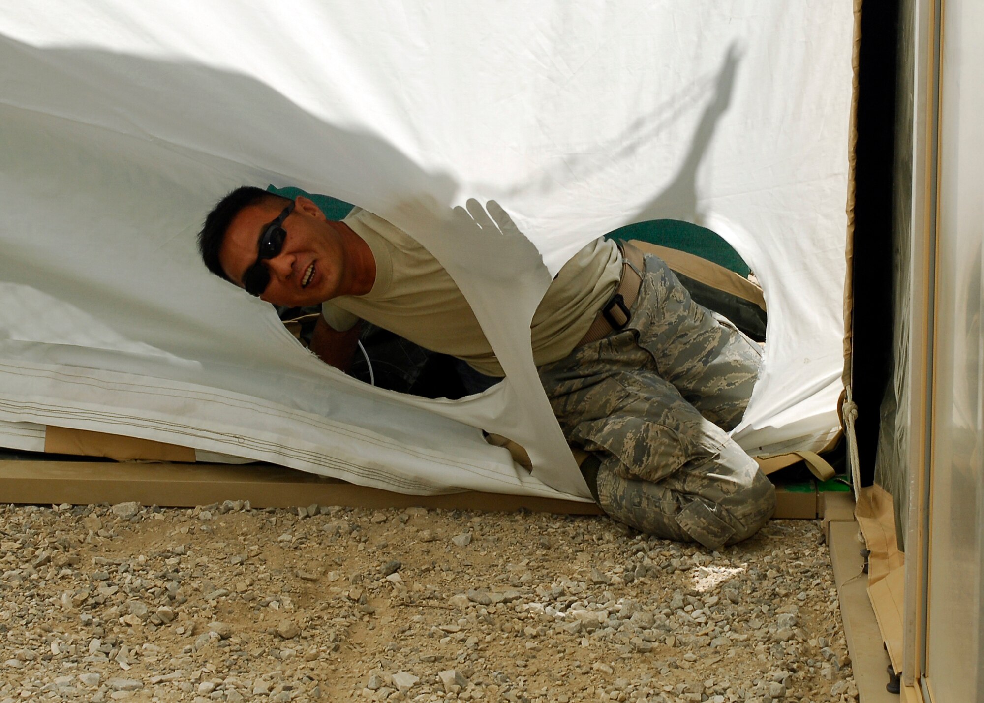 BAGRAM AIRFIELD, Afghanistan -- Master Sgt. Moo Kim, from 455th Expeditionary Civil Engineering Squadron, holds his weight on the side of the fire guard in order for it to be secured to the California Tent structure here, Sept. 3, 2009.  Sergeant Kim is deployed from Yokota Air Base, Japan, and hails from San Antonio, Texas.  This tent is being placed behind the supply yard for extra storage, but usually special permission is needed for the ECES to put together tents.  (U.S. Air Force photo/Senior Airman Felicia Juenke)