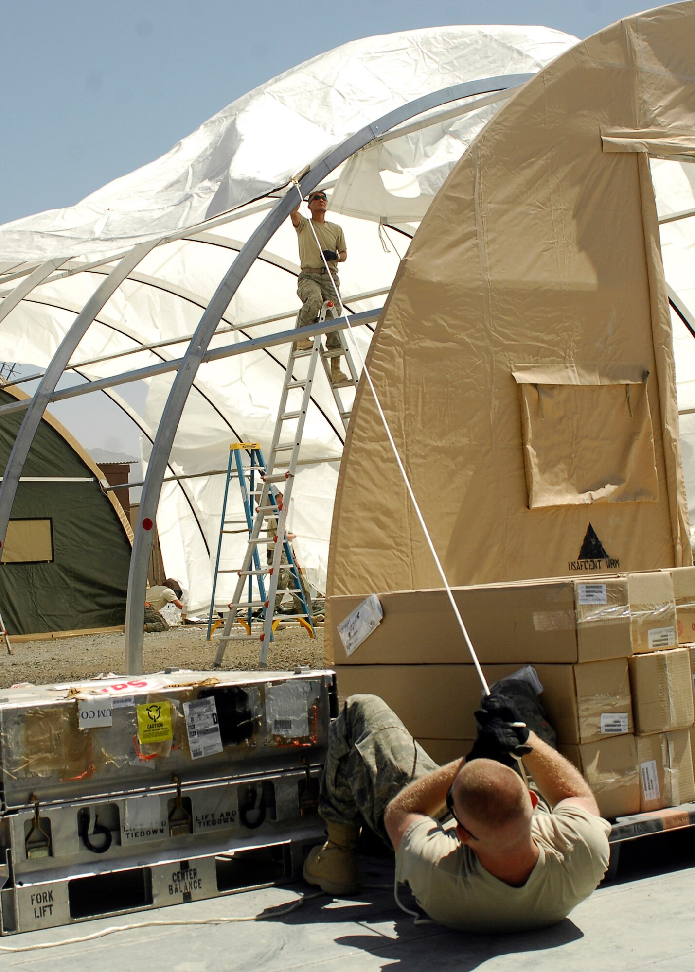 BAGRAM AIRFIELD, Afghanistan -- Senior Airman Mike Davis (ground) helps pull a fire guard onto the California Tent, while Master Sgt. Moo Kim (ladder) ensures that the cover goes smoothly over the bars here, Sept 3, 2009. Both Airmen are Engineering Assistants from 455th Expeditionary Civil Engineering Squadron.   Airman Davis, an Illinois native, is deployed from the Illinois Air National Guard.  Sergeant Kim is deployed from Yokota Air Base, Japan, and hails from San Antonio, Texas.  (U.S. Air Force photo/Senior Airman Felicia Juenke)