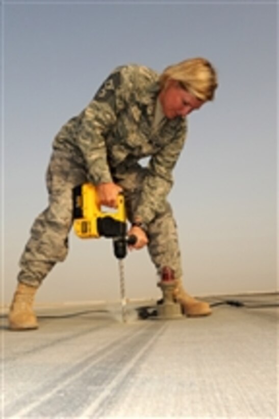 U.S. Air Force Chief Master Sgt. Suzan Sangster, a command chief with the 380th Air Expeditionary Wing, helps airmen of the 380th Expeditionary Civil Engineer Squadron drill holes in concrete to install runway lights in Southwest Asia on Aug. 15, 2009.  