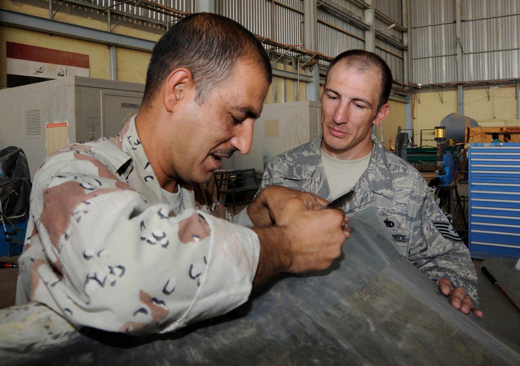 NEW AL MUTHANNA AIR BASE, Iraq -- Tech. Sgt. William Kusar, aircraft structural maintenance and metals technician advisor assigned to the 321st Air Expeditionary Advisor Squadron, observes and advises an Iraqi airman performing a composite repair on a C-130 life raft tub here Sept. 5, 2009. Sergeant Kusar's training ensures the Iraqi airmen will be fully capable of performing structural repairs on their C-130 aircraft. Sergeant Kusar is deployed from Charleston Air Force Base, S.C. (U.S. Air Force photo/Tech. Sgt. Johnny L. Saldivar)