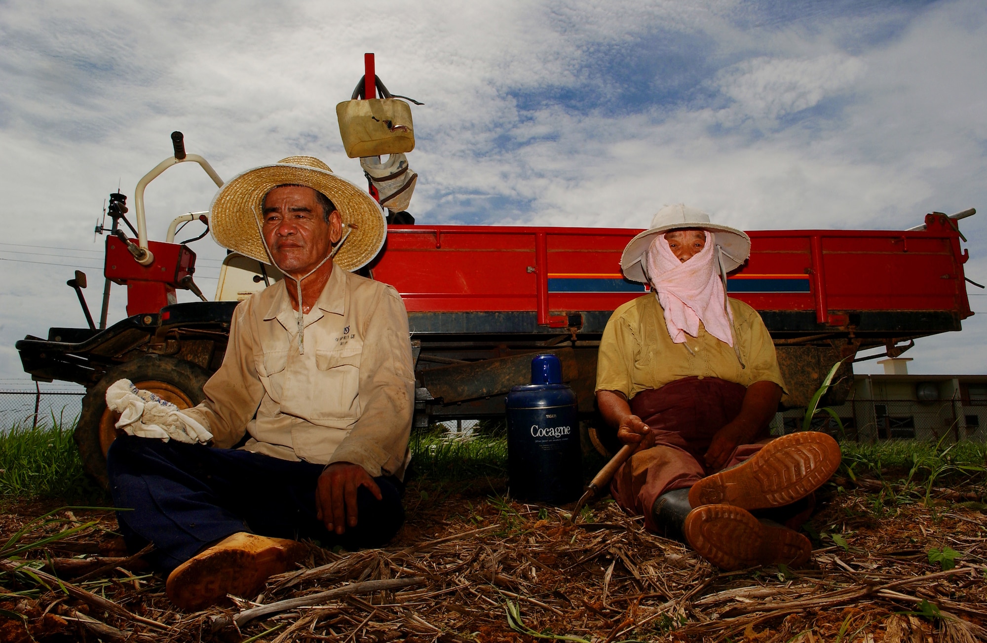A tacit farmer couple takes a brief moment to rest from the summer heat and humidity after working in the sugarcane field. Soon the day will end and tomorrow they'll begin where they left off, devoting themselves to the cultivation of their crops in an area fenced-in and well-guarded.   (U.S. Air Force photo/Tech. Sgt. Rey Ramon)    