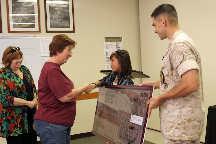 Jayda Kroell recieves a check for $100 at the Provost Marshal’s Office here Sept. 11. Jayda was named the Good Samaritan/Neighbor Program award winner for returning over six dollars in change after shopping at the Marine Mart.